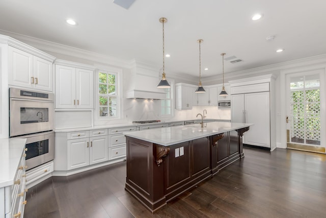 kitchen featuring tasteful backsplash, a kitchen bar, white cabinetry, a kitchen island with sink, and appliances with stainless steel finishes