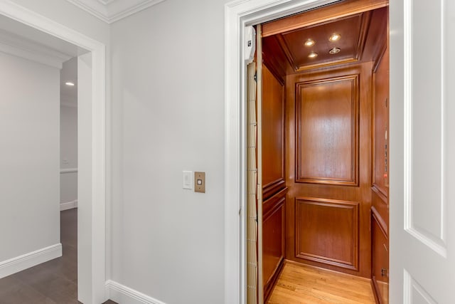 corridor featuring elevator, ornamental molding, and light hardwood / wood-style flooring