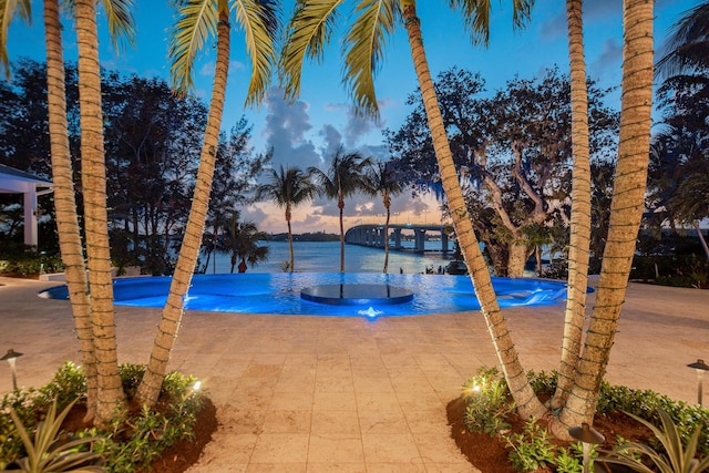 pool at dusk with a patio area and a water view