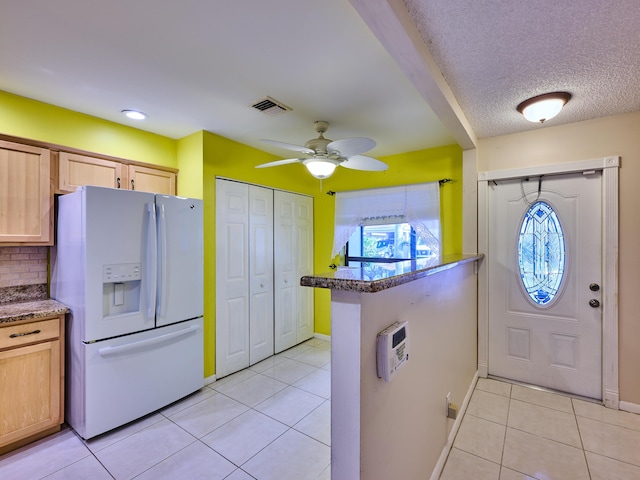 kitchen featuring white refrigerator with ice dispenser, light tile patterned floors, a textured ceiling, and light brown cabinets