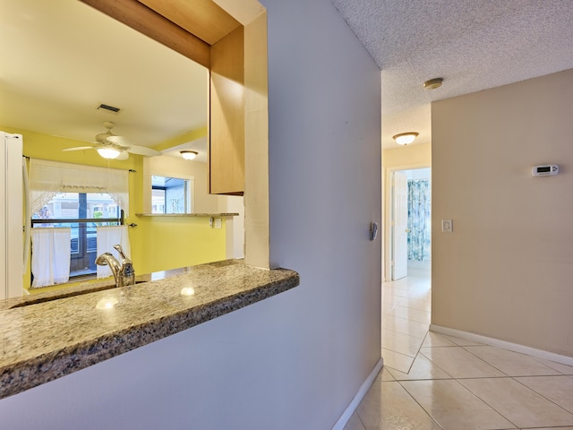 kitchen featuring light tile patterned floors, sink, ceiling fan, a textured ceiling, and stone countertops