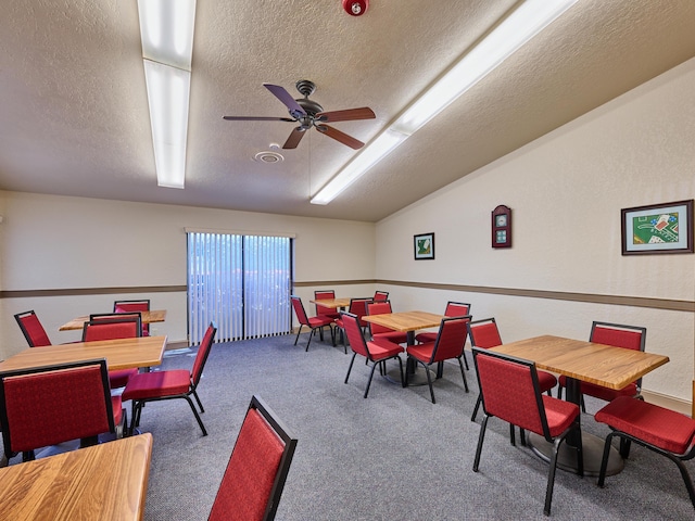 carpeted dining space with lofted ceiling, a textured ceiling, and ceiling fan