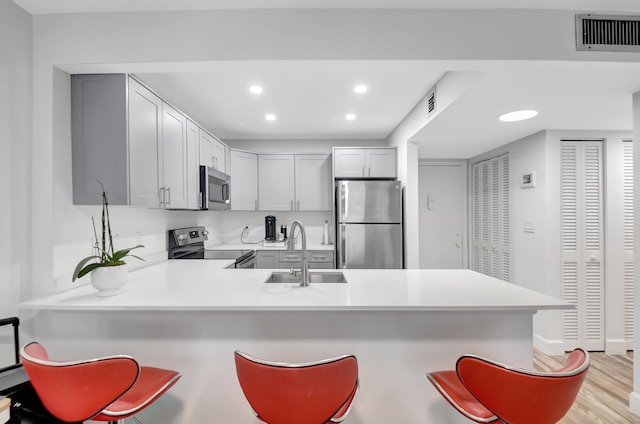 kitchen featuring kitchen peninsula, appliances with stainless steel finishes, sink, a breakfast bar, and light hardwood / wood-style floors