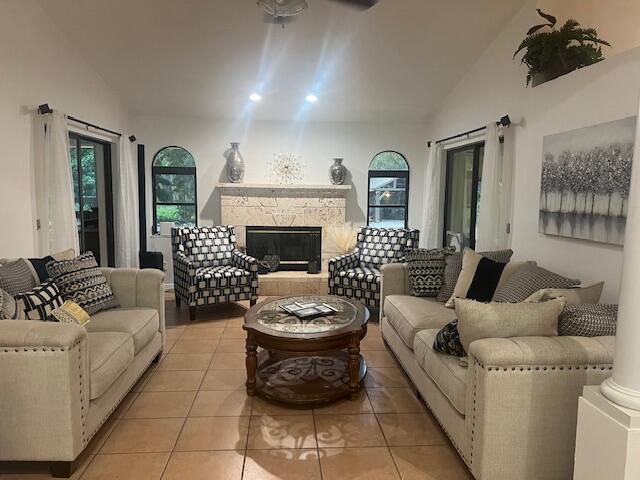 living room featuring light tile patterned floors, vaulted ceiling, a stone fireplace, and ornate columns