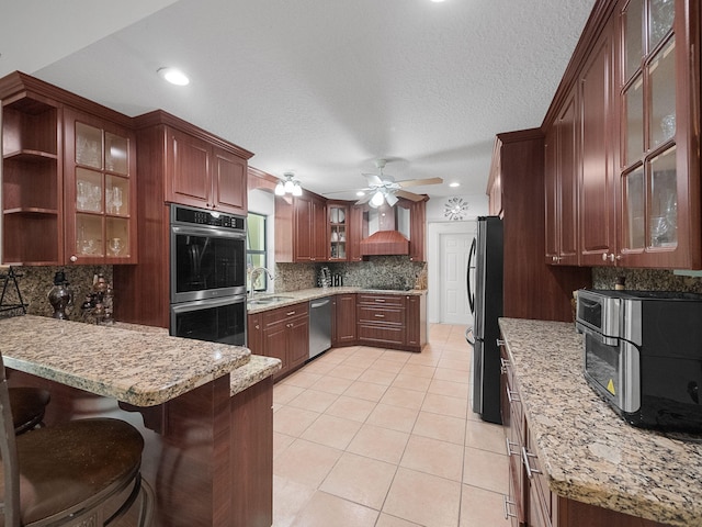 kitchen with sink, custom exhaust hood, light tile patterned floors, appliances with stainless steel finishes, and kitchen peninsula