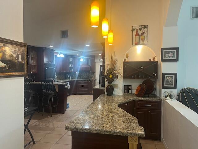 kitchen with decorative light fixtures, light tile patterned floors, a kitchen bar, and dark brown cabinets