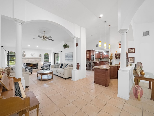 tiled living room featuring ceiling fan, high vaulted ceiling, and decorative columns