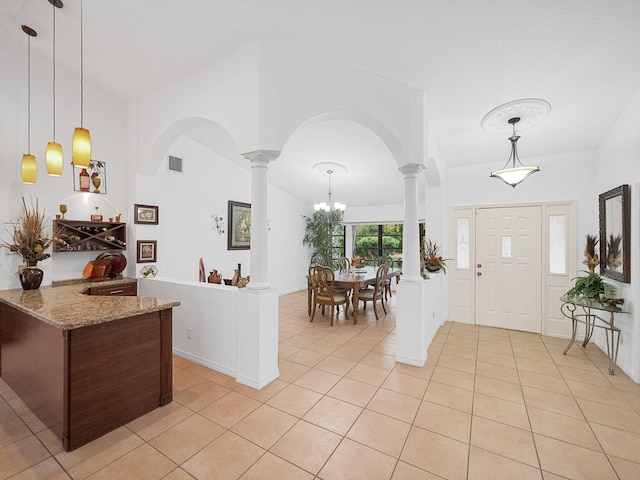 foyer entrance featuring an inviting chandelier, vaulted ceiling, light tile patterned flooring, and ornate columns