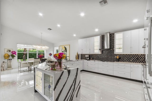 kitchen featuring white cabinetry, wall chimney range hood, hanging light fixtures, a chandelier, and vaulted ceiling