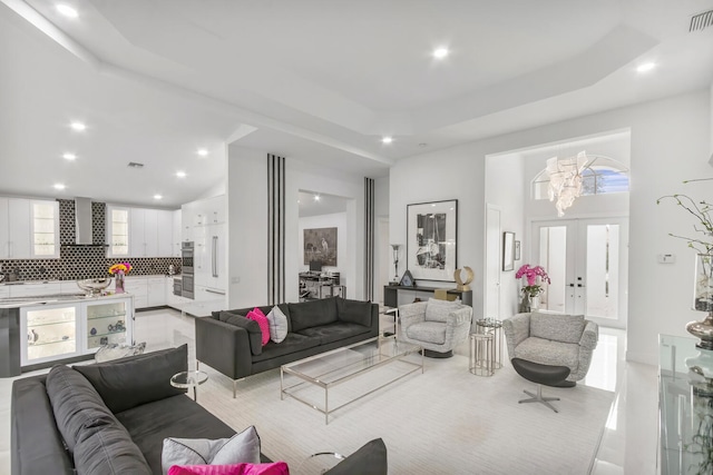 living room with a raised ceiling, french doors, and an inviting chandelier