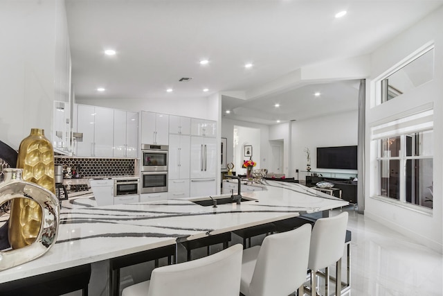 kitchen featuring white cabinets, double oven, decorative backsplash, sink, and vaulted ceiling