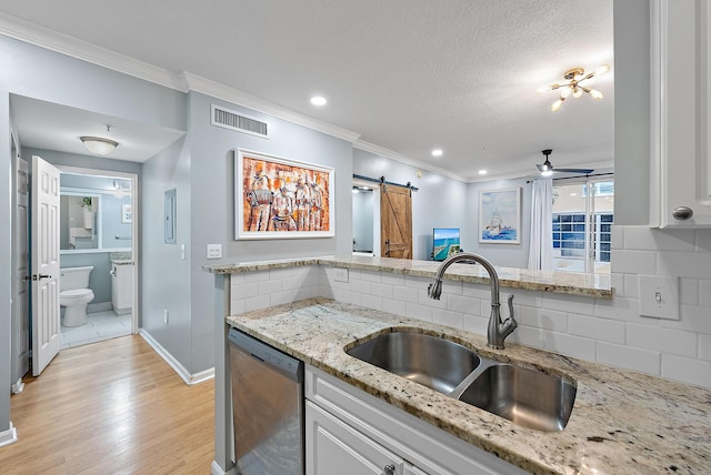 kitchen featuring a barn door, backsplash, dishwasher, sink, and light stone counters