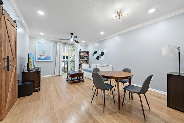 dining area featuring ceiling fan, a barn door, crown molding, light wood-type flooring, and a textured ceiling