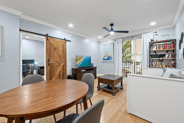 dining room with ceiling fan, light hardwood / wood-style flooring, ornamental molding, and a barn door