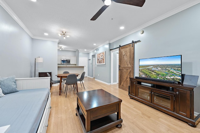 living room with ceiling fan, a barn door, crown molding, and light hardwood / wood-style flooring