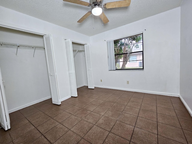 unfurnished bedroom featuring a textured ceiling, ceiling fan, multiple closets, and dark tile patterned floors