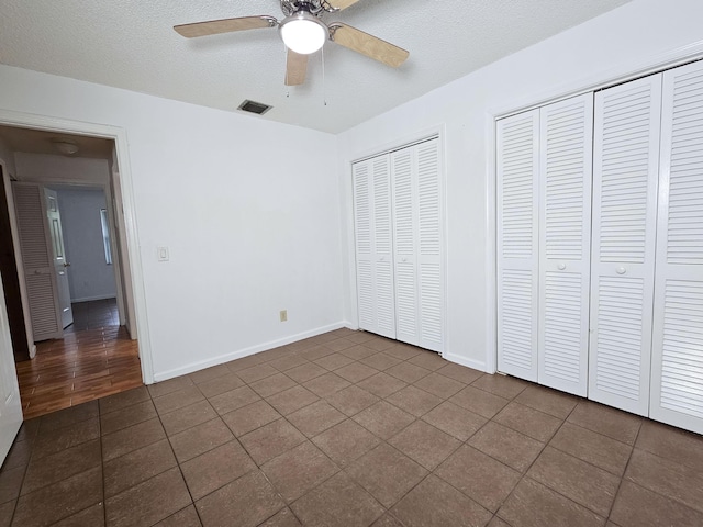 unfurnished bedroom with ceiling fan, two closets, a textured ceiling, and tile patterned flooring