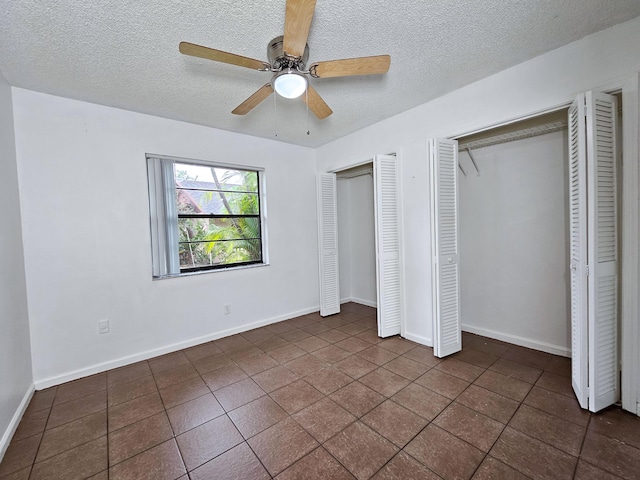 unfurnished bedroom featuring a textured ceiling, ceiling fan, dark tile patterned flooring, and multiple closets