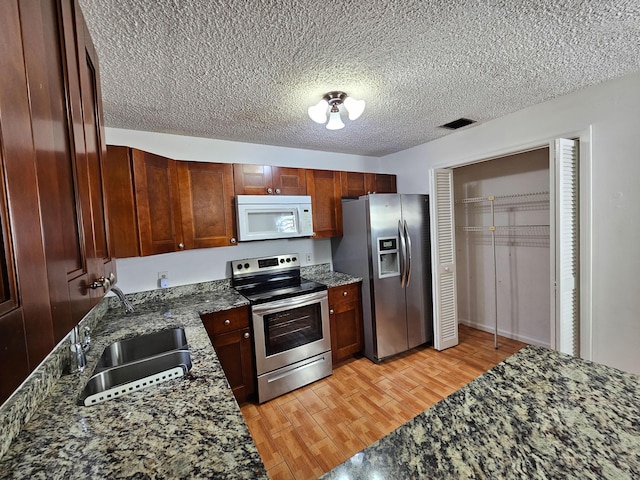 kitchen featuring stainless steel appliances, light wood-type flooring, dark stone counters, a textured ceiling, and sink