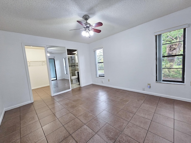 unfurnished bedroom featuring ceiling fan, a spacious closet, ensuite bathroom, and multiple windows