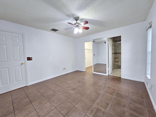 unfurnished bedroom with ceiling fan, connected bathroom, a closet, a textured ceiling, and a walk in closet