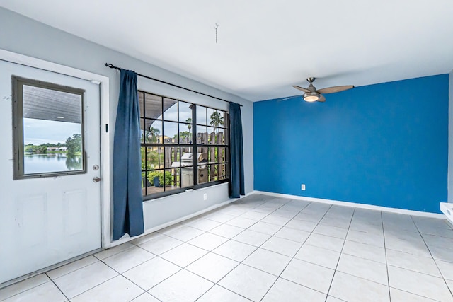 tiled empty room featuring ceiling fan and a water view