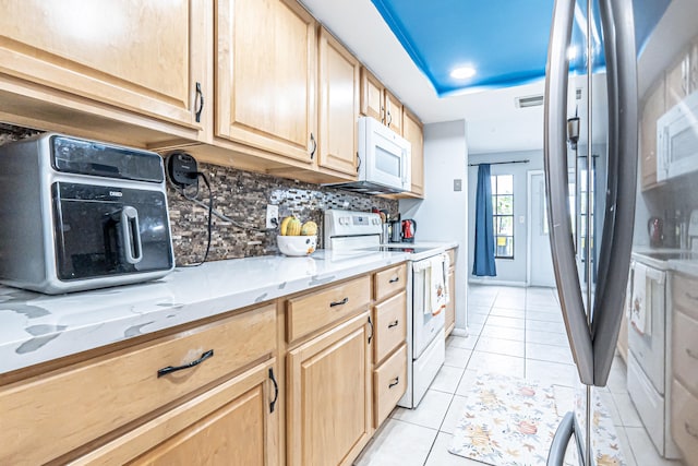 kitchen with light tile patterned floors, backsplash, light brown cabinets, white appliances, and light stone countertops