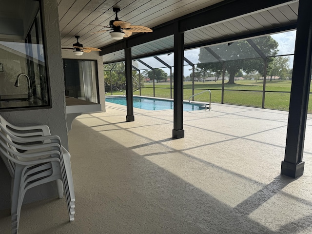 pool with a patio, a lawn, glass enclosure, ceiling fan, and a sink