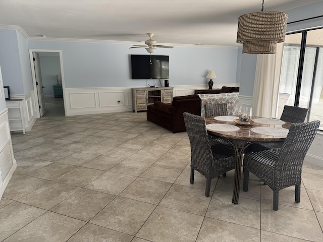 dining area with ceiling fan, a wainscoted wall, light tile patterned flooring, and crown molding