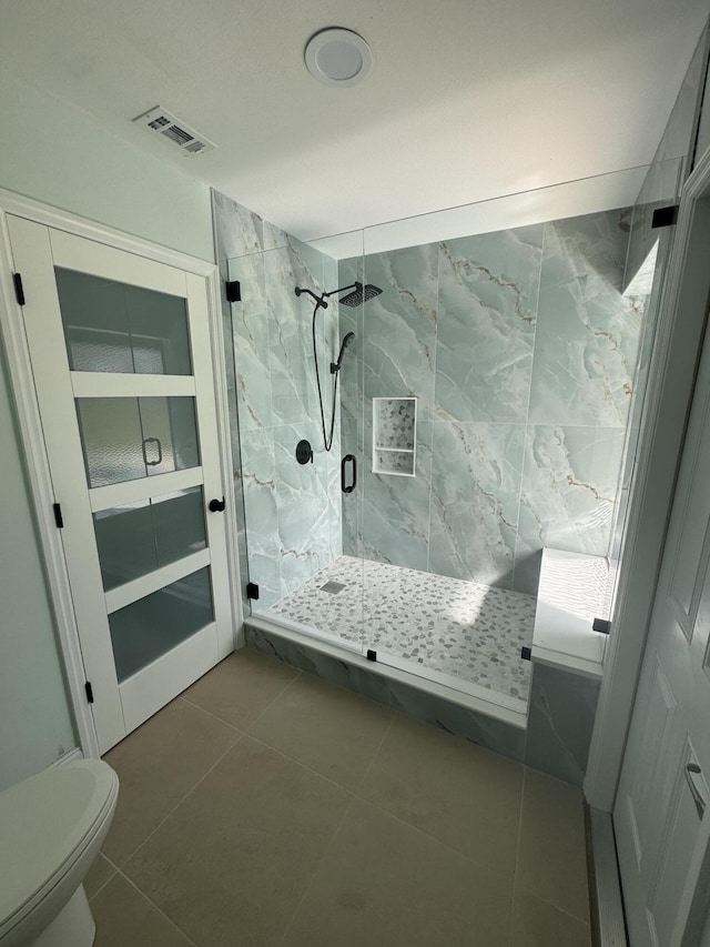 bathroom featuring visible vents, toilet, a marble finish shower, and tile patterned floors