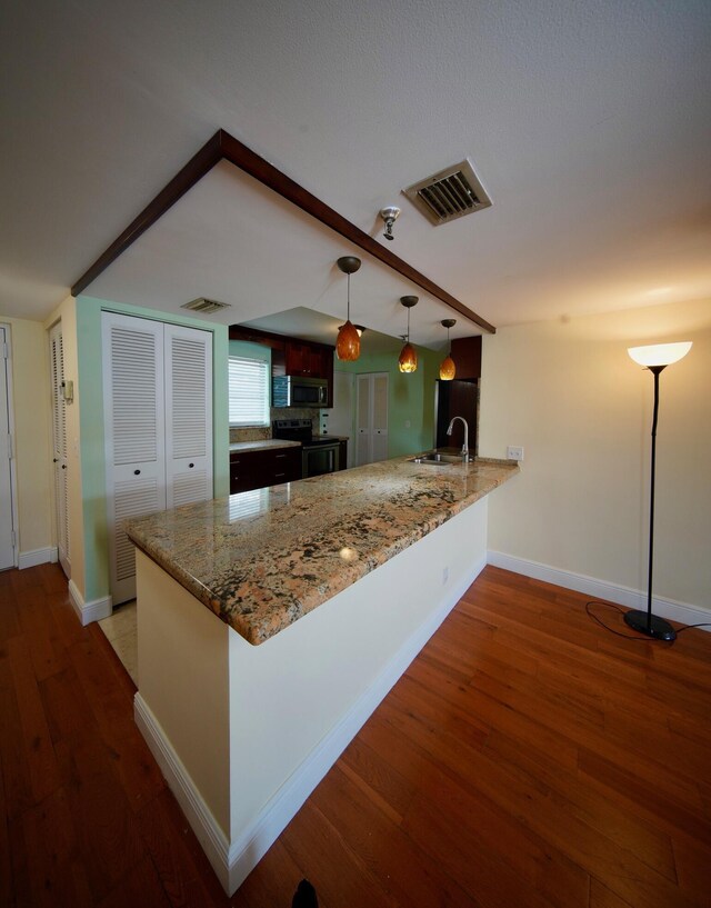 kitchen featuring decorative light fixtures, dark stone countertops, kitchen peninsula, sink, and appliances with stainless steel finishes