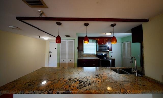 kitchen with appliances with stainless steel finishes, stone counters, a sink, and pendant lighting