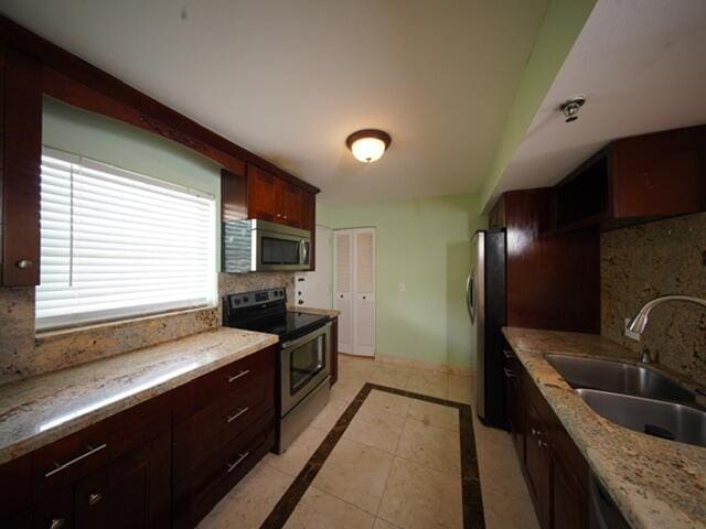 kitchen with stainless steel appliances, a sink, backsplash, and light stone counters