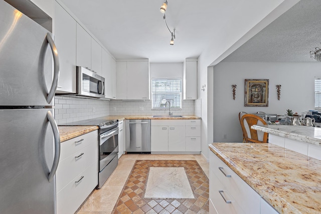 kitchen with white cabinets, stainless steel appliances, decorative backsplash, sink, and rail lighting