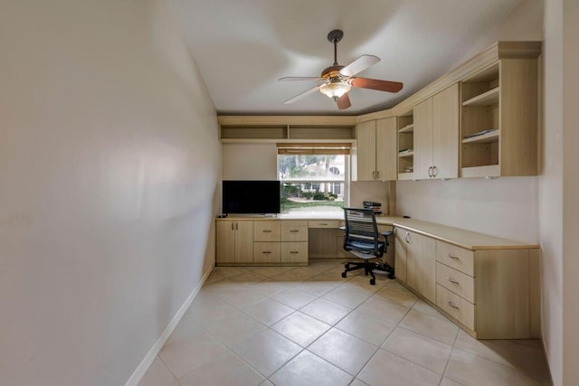 unfurnished office with built in desk, ceiling fan, and light tile patterned flooring