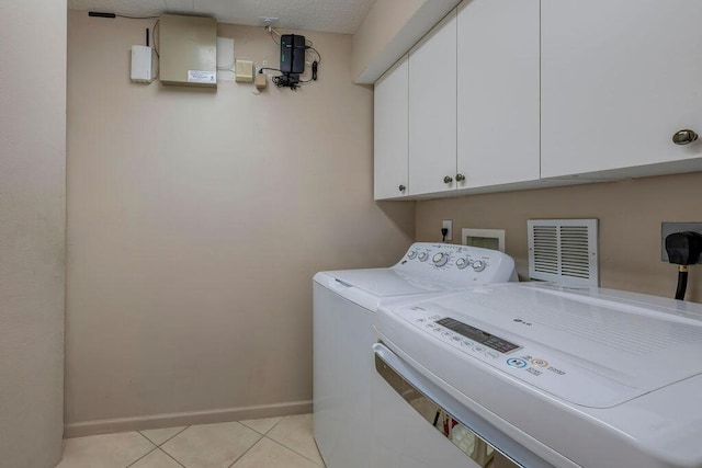 clothes washing area with light tile patterned floors, washer and clothes dryer, and cabinets