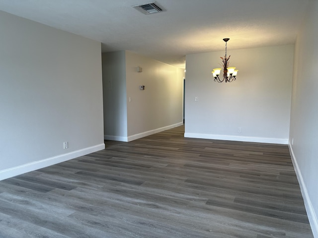 unfurnished room featuring dark wood-type flooring and a notable chandelier