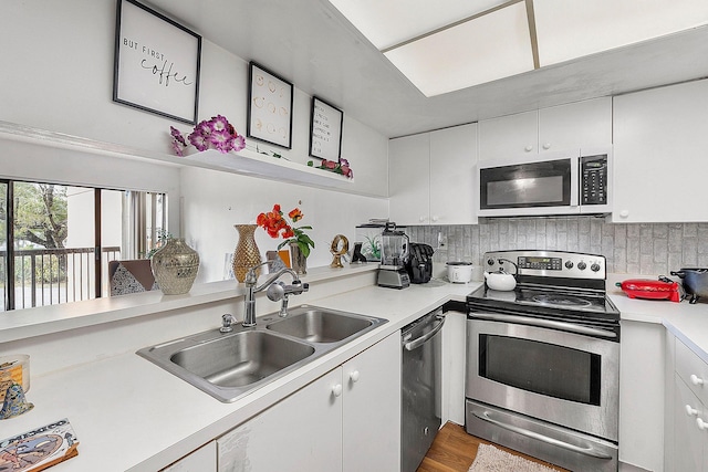 kitchen featuring appliances with stainless steel finishes, tasteful backsplash, wood-type flooring, white cabinetry, and sink