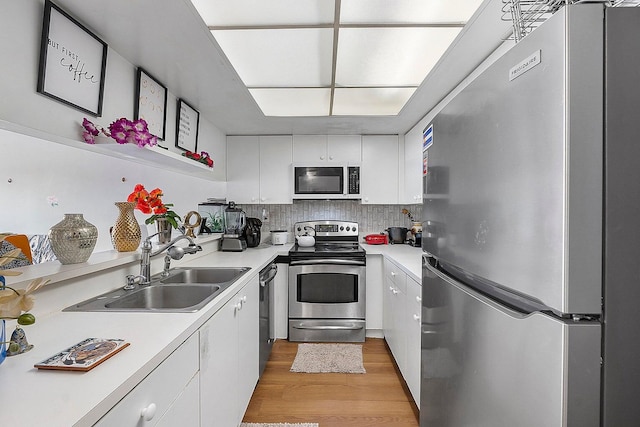 kitchen featuring appliances with stainless steel finishes, white cabinetry, light hardwood / wood-style floors, sink, and decorative backsplash