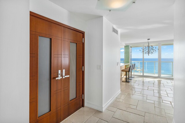 corridor with an inviting chandelier, a water view, and expansive windows