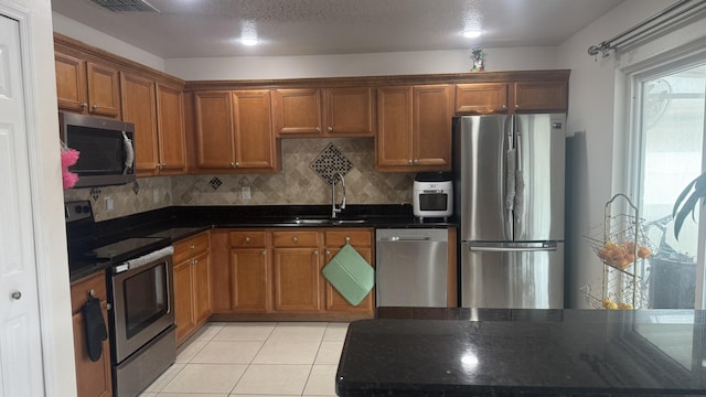 kitchen featuring tasteful backsplash, sink, dark stone countertops, light tile patterned floors, and stainless steel appliances