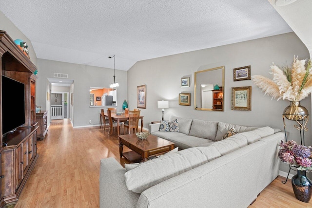 living room featuring a textured ceiling, light hardwood / wood-style flooring, and lofted ceiling