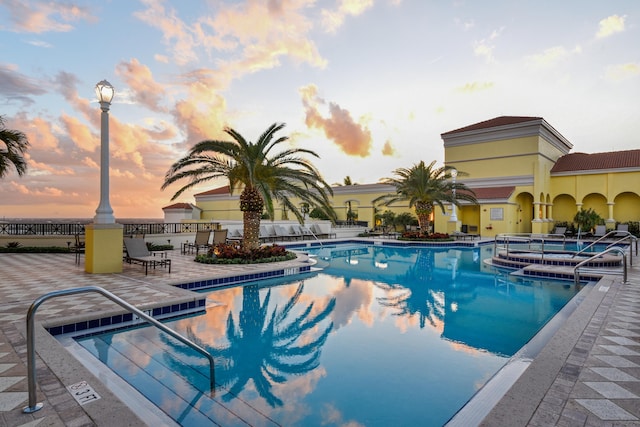 pool at dusk featuring a patio area and a hot tub