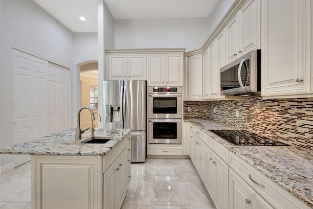 kitchen featuring a center island with sink, stainless steel appliances, tasteful backsplash, light stone countertops, and sink