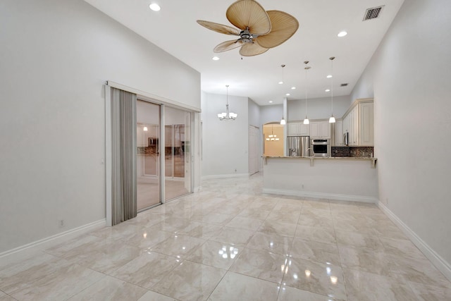 unfurnished living room featuring a towering ceiling and ceiling fan with notable chandelier