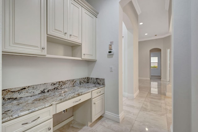 kitchen featuring white cabinetry, built in desk, ornamental molding, and light stone countertops