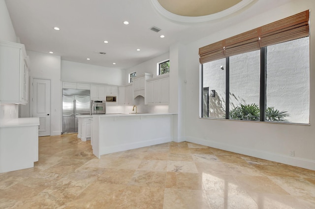 kitchen featuring kitchen peninsula, a high ceiling, built in appliances, white cabinets, and sink