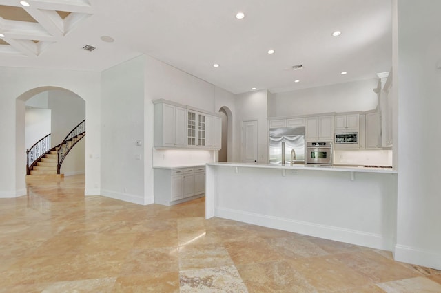 kitchen featuring a breakfast bar, kitchen peninsula, a towering ceiling, built in appliances, and coffered ceiling