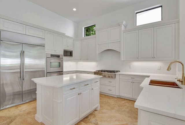 kitchen with a center island, built in appliances, wall chimney exhaust hood, white cabinets, and sink