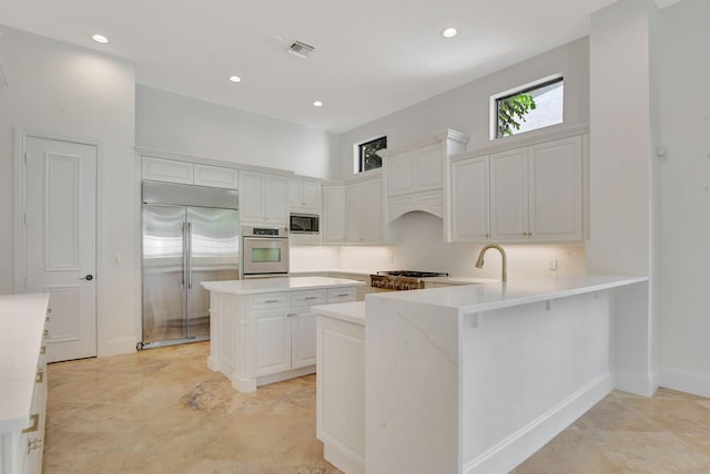 kitchen featuring kitchen peninsula, stainless steel appliances, white cabinetry, and a kitchen island